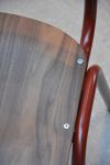 Detailaufnahme des Vintagestuhls ZERO von Jan Kurtz aus dunklem Walnussholz mit rubinrotem Stahlgestell: auf der Sitzfläche ist die lebendige Maserung des Holzes deutlich sichtbar Vintagestuhl aus Stahl in rubinrot und Holz in Walnuss - ZERO von Jan Kurtz